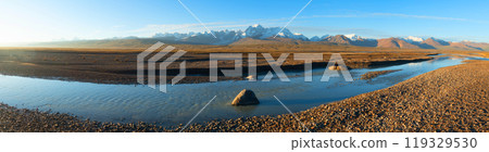 A blue transparent river meanders among the rocks in a picturesque valley of the mountain range. In the background, a majestic mountain range can be seen rising above the landscape. A blue transparent river meanders among the rocks in a picturesque valley of the mountain range. In the background, a majestic mountain range can be seen rising above the landscape. 119329530