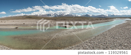 A blue transparent river meanders among the rocks in a picturesque valley of the mountain range. In the background, a majestic mountain range can be seen rising above the landscape. A blue transparent river meanders among the rocks in a picturesque valley of the mountain range. In the background, a majestic mountain range can be seen rising above the landscape. 119329561
