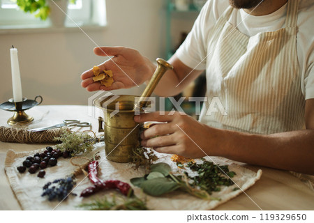 Side view of man adds dried rose petals to a mortar and pestle. Homemade healthy and nutrition supplements Side view of man adds dried rose petals to a mortar and pestle. Homemade healthy and nutrition supplements 119329650