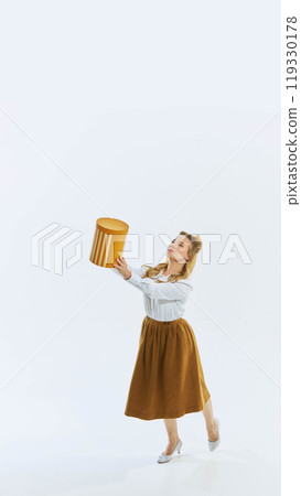 Elegant young woman in retro-style outfit holding large golden box in excited pose, she is about to present surprise, capturing joy and anticipation. 119330178