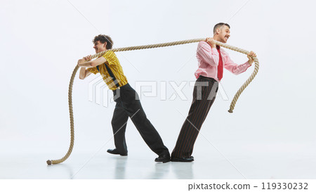 Two men engaged in tug of war, one pulling rope with all his strength while other in resistance, showing competitive spirit. 119330232