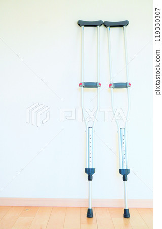 Crutches leaning against a white wall on a wooden floor indoors 119330307