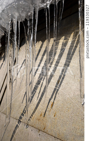 Beautiful spring icicles dripping down from snow covered roof along metal wall. Vertical format. 119330327