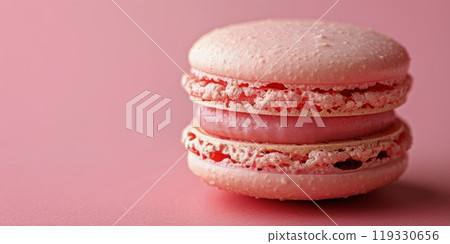 Delicate pink macaron resting on a pastel surface with scattered crumbs and decorations 119330656
