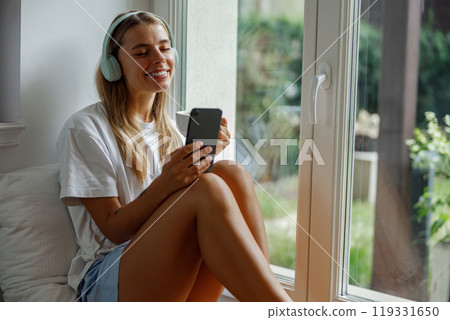 Relaxing Moment A Young Woman Featuring Enjoyment of Music While Resting By The Window 119331650