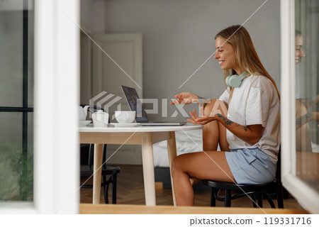 A young woman works diligently on her laptop at home, immersed in tasks while wearing headphones A young woman works diligently on her laptop at home, immersed in tasks while wearing headphones 119331716