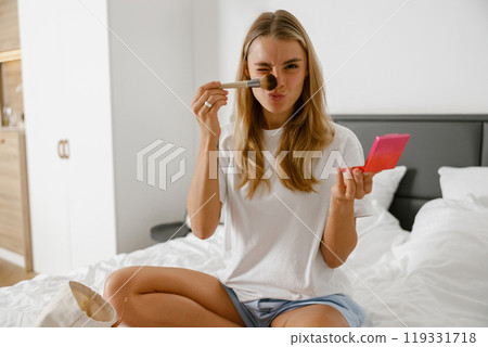 A young woman enjoys her vibrant lifestyle while applying makeup at home in a casual routine 119331718
