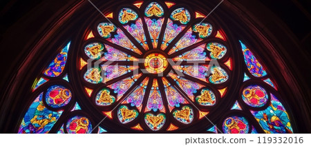 Stunning kaleidoscopic stained glass rose window in a cathedral, featuring intricate patterns of hearts and floral designs in vibrant colors 119332016