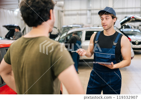Portrait of mechanic male in uniform explaining checklist car maintenance and repair to unrecognizable man client at vehicle repair shop. Repairman with clipboard talking to man or owner at car shop. 119332907