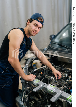 Vertical portrait of confident mechanic male examining car engine in auto repair shop, looking at camera with serious expression. Skilled repairman inspecting car engine in garage vehicle service. Vertical portrait of confident mechanic male examining car engine in auto repair shop, looking at camera with serious expression. Skilled repairman inspecting car engine in garage vehicle service. 119332915