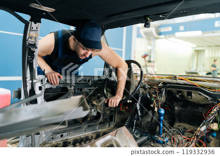 View from interior of old vehicle to skilled mechanic in blue overalls inspecting car wiring after removing dashboard, showing expertise in troubleshooting automotive problems. Concept of car repair 119332936