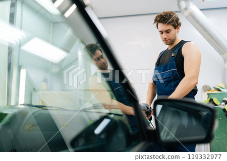 Muscular mechanic in uniform polish auto hood using grinding unit in automobile repair and renew service station. Repair after accident. Concept of professional car repair and maintenance work. Muscular mechanic in uniform polish auto hood using grinding unit in automobile repair and renew service station. Repair after accident. Concept of professional car repair and maintenance work. 119332977