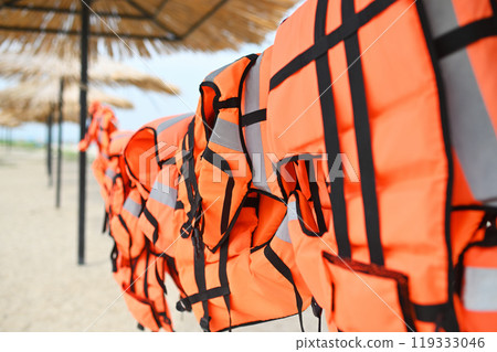 lots of orange life jackets on the background of sand, sea and straw umbrellas. High quality 4k footage 119333046