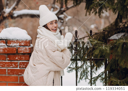 Happy smiling young woman portrait dressed coat scarf hat and mittens enjoys winter weather at pine winter park Happy smiling young woman portrait dressed coat scarf hat and mittens enjoys winter weather at pine winter park 119334051