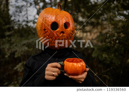 Positive smiling woman with pumpkin head for Halloween drinking tea or coffee from orange mug. Jack-o-lantern costume.Trick or treat. 119336560