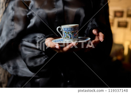 An Elegant Porcelain Teacup is Gracefully Held Against a Beautifully Dim Lighting Background 119337148