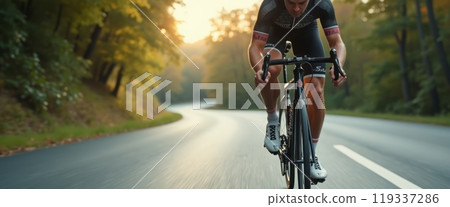 A cyclist rides a road bike down a sunlit road surrounded by trees during sunrise, capturing the essence of freedom and adventure. The image showcases cycling and nature. 119337286