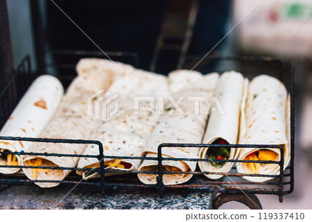 Flatbreads rolled and filled with cheese and vegetables. BBQ cooking preparation process outdoors. Vegetarian street food on a metal grid up close. Flatbreads rolled and filled with cheese and vegetables. BBQ cooking preparation process outdoors. Vegetarian street food on a metal grid up close. 119337410