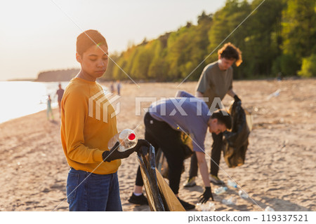 Earth day. Volunteers activists team collects garbage cleaning of beach coastal zone. Woman puts plastic bottle trash in garbage bag on ocean shore. Environmental conservation coastal zone cleaning Earth day. Volunteers activists team collects garbage cleaning of beach coastal zone. Woman puts plastic bottle trash in garbage bag on ocean shore. Environmental conservation coastal zone cleaning 119337521