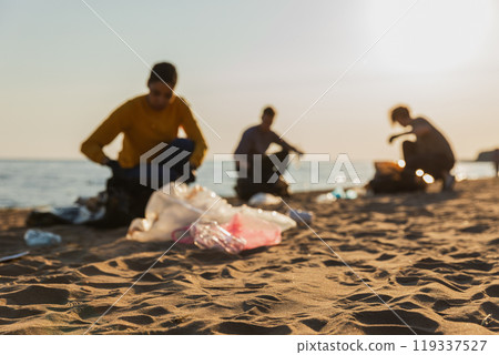 Earth day. Volunteers activists collects garbage cleaning of beach coastal zone. Woman mans with trash in garbage bag on ocean shore. Environmental conservation coastal zone cleaning. Blurred image Earth day. Volunteers activists collects garbage cleaning of beach coastal zone. Woman mans with trash in garbage bag on ocean shore. Environmental conservation coastal zone cleaning. Blurred image 119337527