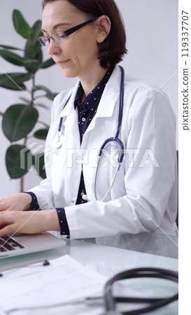 Doctor woman is working with laptop computer at the glass table in clinic. Physician is typing medical information or giving advices online. Medicine and pharmacy 119337707