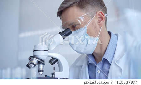 Man scientist with protective glasses, mask and gloves is using microscope in laboratory, portrait of researcher. Microbiology science concept Man scientist with protective glasses, mask and gloves is using microscope in laboratory, portrait of researcher. Microbiology science concept 119337974