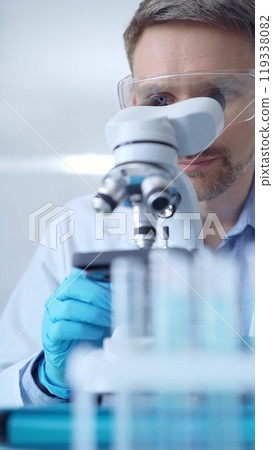 Man scientist with protective glasses and gloves is using microscope in laboratory, vertical portrait of researcher. Microbiology science concept Man scientist with protective glasses and gloves is using microscope in laboratory, vertical portrait of researcher. Microbiology science concept 119338082