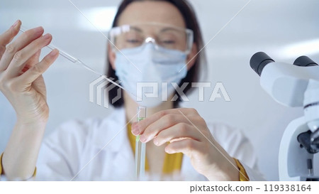 Woman with safety glasses and blue mask is working with lab tube 119338164