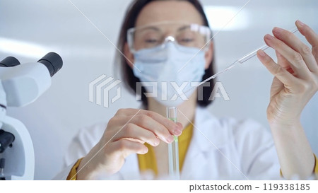 Woman with safety glasses and blue mask is working with lab tubes using a pipette in a modern laboratory, close-up of researcher. Science and medicine 119338185