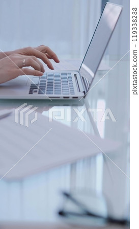 Business woman is working with laptop computer while sitting at the glass table in home office, closeup of hands Business woman is working with laptop computer while sitting at the glass table in home office, closeup of hands 119338288