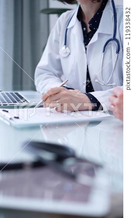 Doctor and patient. Female physician is sitting at the glass table, listening a senior man and writing medication history records. Medicine concept 119338432