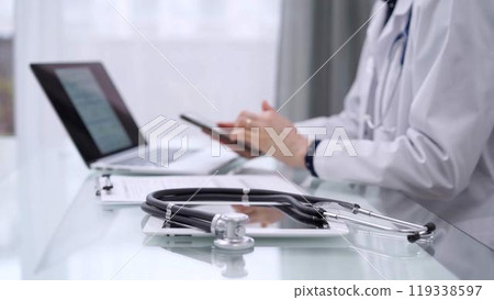 Stethoscope and clipboard are lying on the glass table while doctor woman is using a smartphone at the background. Medicine concept 119338597