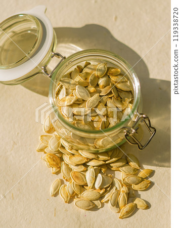 Open glass jar with raw pumpkin seeds on beige background . High quality photo Open glass jar with raw pumpkin seeds on beige background . High quality photo 119338720