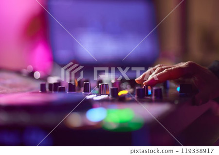 control DJ for mixing music with blurred people dancing at party in nightclub. 119338917