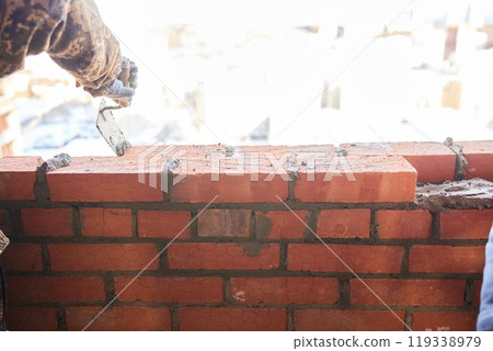 professional construction worker laying bricks and building barbecue in industrial site. Detail of hand adjusting bricks 119338979