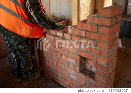 professional construction worker laying bricks and building barbecue in industrial site. Detail of hand adjusting bricks 119338997
