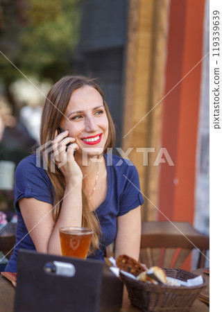 Smiling woman talking on a phone at a cafe surrounded by flowers Smiling woman talking on a phone at a cafe surrounded by flowers 119339639
