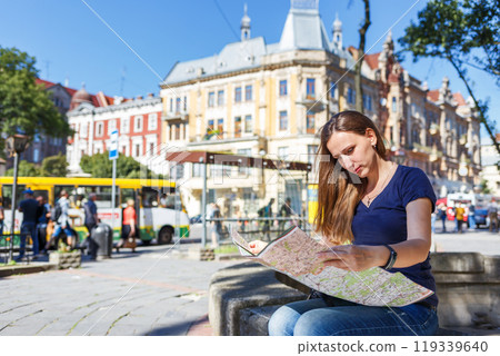 Young woman exploring a city map on a sunny day in a vibrant location 119339640