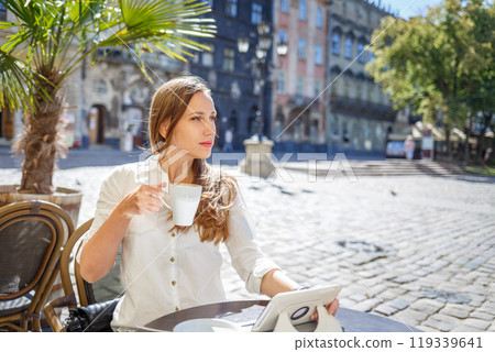 Young woman enjoying coffee at a charming cafe in the heart of a historic town square 119339641