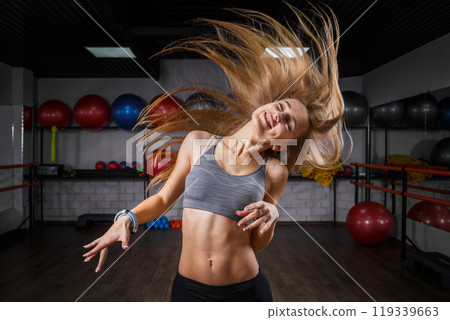 Energetic young woman dancing with enthusiasm in a gym during fitness class session 119339663
