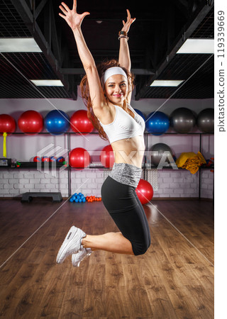 Woman performing a joyful energetic dance leap in a fitness studio with exercise balls 119339669