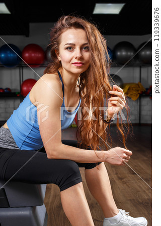 Woman with long hair sitting on step in fitness center during workout session 119339676