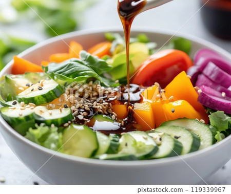 Fresh vegetable salad in a white bowl with a flavorful dressing being drizzled on top, featuring vibrant colors and textures, perfect for healthy meal options. 119339967