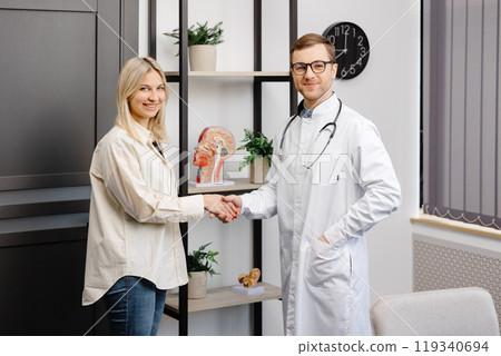 Vertical shot of young happy cheerful medical worker therapist in white doctor's robe having appointment consulting female patient in modern clinic hospital. Medical healthcare concept Vertical shot of young happy cheerful medical worker therapist in white doctor's robe having appointment consulting female patient in modern clinic hospital. Medical healthcare concept 119340694