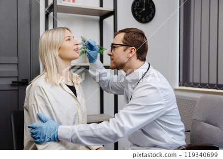 A young attractive otolaryngologist examining nose of a young patient during a medical examination in the ENT office 119340699