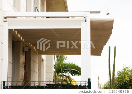 Attached pergola on a villa in Spain. A modern or classic hotel on the tropical resort. White wooden long courtyard canopy over house entrance, cottage. Front door canopies. 119340826