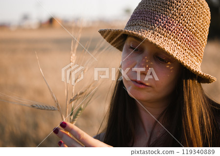 Beautiful white young woman in straw hat picking wheat ears in a field. Growing crops, farming, harvesting in summer. Human and nature, harmony concept. Dreamy pretty relaxed girl in summertime. Beautiful white young woman in straw hat picking wheat ears in a field. Growing crops, farming, harvesting in summer. Human and nature, harmony concept. Dreamy pretty relaxed girl in summertime. 119340889