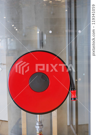 A striking red fire hose reel stands out against a contemporary and modern background setting 119341059