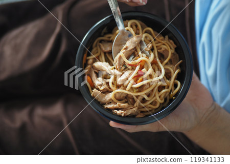 A bowl of delicious chicken noodles rests on a cozy blanket, with a fork beside it 119341133