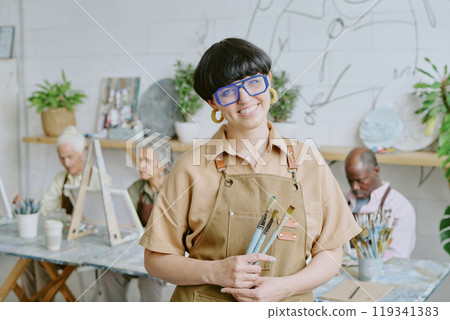 Portrait of young adult Caucasian drawing teacher holding paintbrushes and posing for photo Portrait of young adult Caucasian drawing teacher holding paintbrushes and posing for photo 119341383